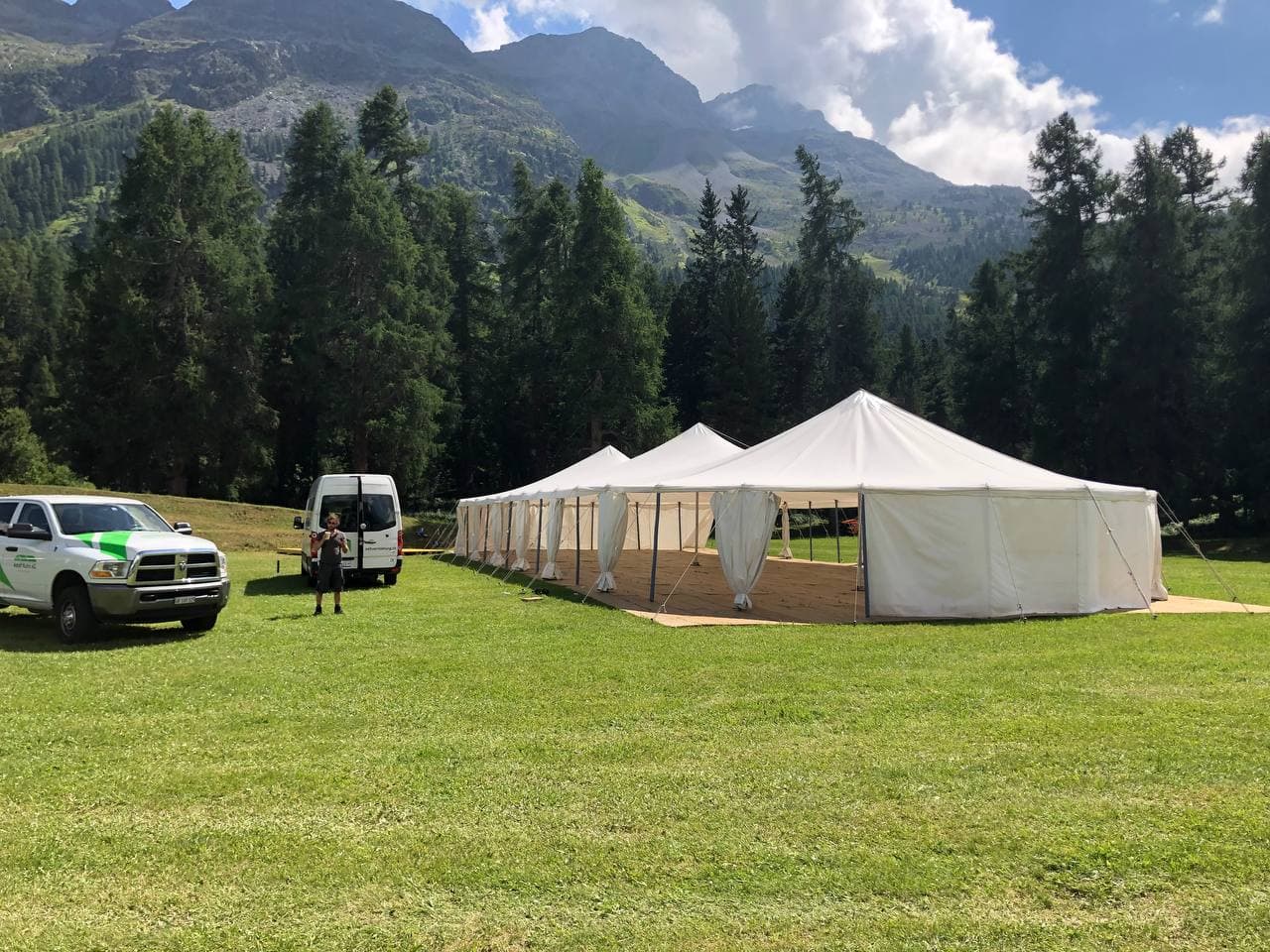 Stoffzelte auf einer Bergwiese mit Lieferwagen beim Aufbau