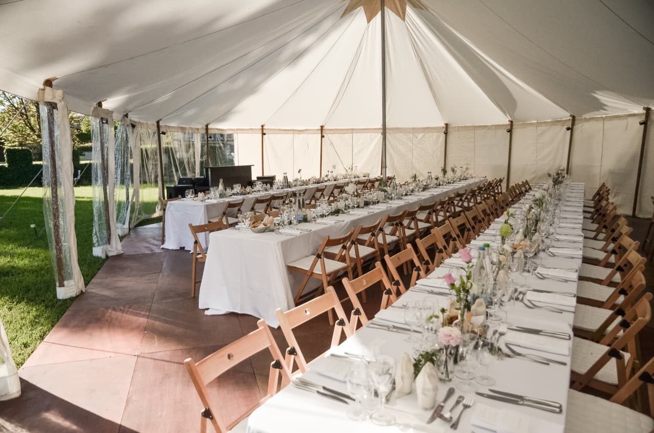 Gedeckte Hochzeitstafel mit Holzstühlen unter einem weissen Stoffzelt